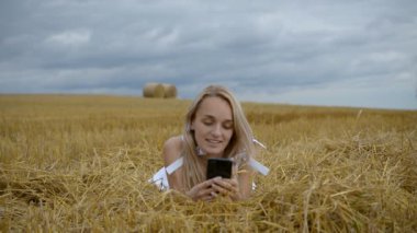 Bir kız buğday tarlasında yatıyor ve telefonuna mesaj yazıyor.