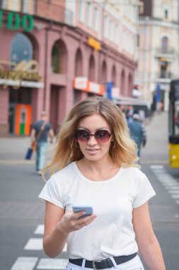 Şehirli caddede cep telefonu ve mesaj kullanan neşeli bir kadın.