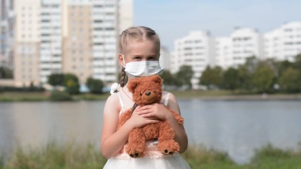 Petite fille dans un masque de protection et un ours en peluche dans ses mains — Video