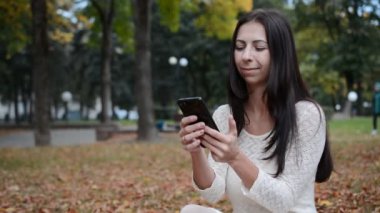 Sonbahar parkında güzel bir esmer kızın portresi. Düşen yapraklara oturur ve bir mesaj yazar.