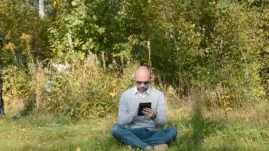 Elinde tabletle ormanda oturan bir müdür.