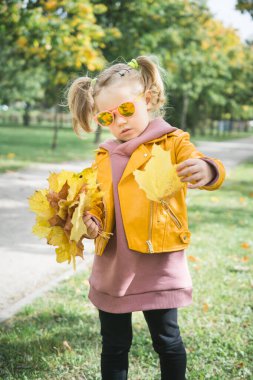 Sonbahar parkında tüylü yapraklarla oynayan üç yaşında küçük bir kız.