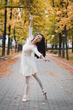 Sonbahar parkında bir fotoğrafçıya poz veren beyaz elbiseli bir kız balerin.