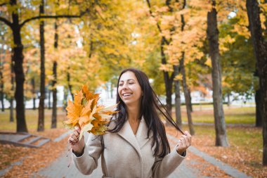Sonbahar parkında güzel bir kız portresi ve ellerinde akçaağaç yaprakları