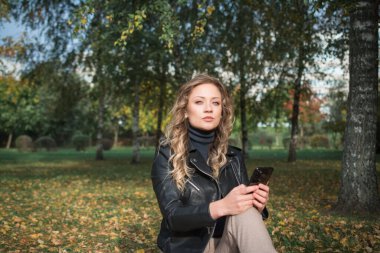 Güz parkında siyah deri ceketli güzel bir kadın.