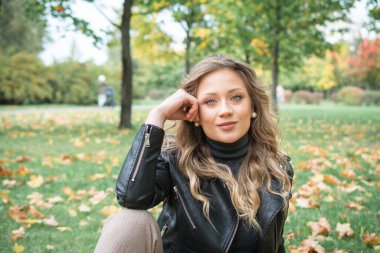 Güz parkında siyah deri ceketli güzel bir kadın.