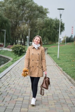 Güzel sarışın kadın sonbahar parkında tek başına yürüyor.