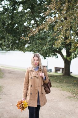 Güzel sarışın kadın sonbahar parkında tek başına yürüyor.