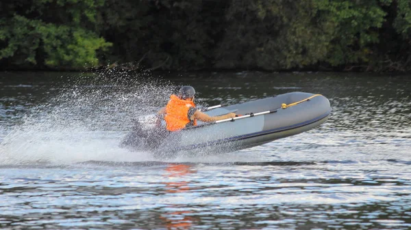 Gray Inflatable outboard motor boat with racer in orange lifejacket and black helmet fast glide floats in water spray on water Race at river on a Sunny summer day, amateur outdoor sport competition — Stock Image Gray Inflatable Outboard Motor Boat Racer Orange Lifejacket Black Helmet Royalty Free Stock Photos