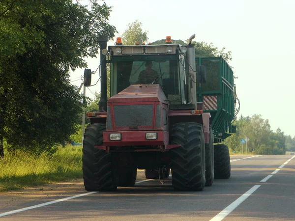田舎アスファルト道路 農村輸送物流 農業ビジネス 農業にロードされた緑のトレーラードライブを持つ大きな赤い重い車輪付きトラクター — ストック写真