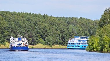 Moskova Bölgesi 'nde Rus seyahati, Moskova Kanal Nehri' nde yüzen iki yolcu gemisi, yaz günü nehir kıyısında yeşil orman ve mavi gökyüzü arka planıyla turist gemisi dikiz görüntüsü.