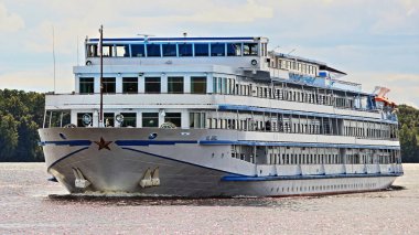 Güzel, büyük bir Rus seyahati dört güverte beyaz yolcu gemisi su üzerinde yüzüyor, turist gemisi yaz günü nehir kıyısında yeşil ağaçlar ve mavi gökyüzü arka planıyla ön cephede.