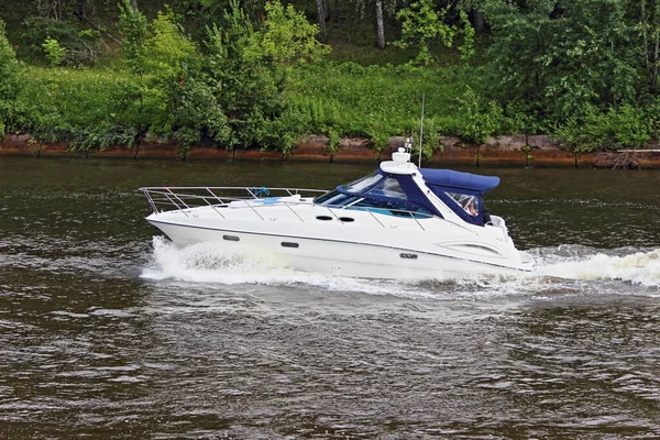 Modern white cabin awning plastic motor boat with inboard motor floats right to left on river water with wake spray, side view on summer day, outdoor powerboat active recreation, water sports