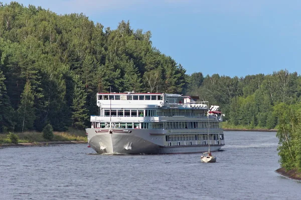 Big Russian white passenger tourist ship floats on water near small private yacht on Moscow river canal on shore forest background on summer day, counter divergence of vessels
