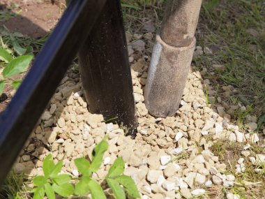 Güneşli bir yaz gününde köyün yakınlarında yeşil çimenlerin arka planına karşı ağır bir tamp barı olan metal çit destek direğinin çakıl taşı tabanını takviye edin.