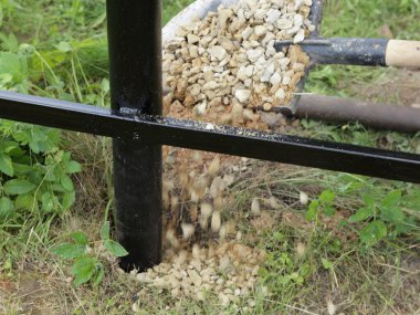 Yeni metal çitin tabanındaki sütunları çakıl taşı ve kürekle güçlendirin.