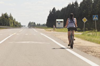 Beyaz kadın bisikletçi yaz kıyafetleri içinde boş bir banliyö otoyolunda bisiklet sürüyor, bisiklet güvenliğiyle geziyor.