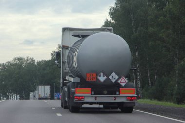 Üzerinde ADR işareti 99 3257 olan gümüş gri Bitumen kamyon tankı yaz günü asfalt yolda yeşil ağaçların arka planında, asfalt taşımada, yanıcı sıvı lojistikte