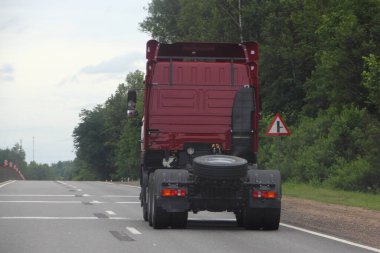 Yazın boş asfalt yolda ilerleyen römorksuz, yeşil orman arka planında manzaralı tek bir Avrupa kırmızı yarı karavan nakliye kamyonu kafası.
