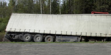 Kurumuş asfaltlı otoyolda, yol kenarındaki hendeğe yakın eğilmiş bir tır.
