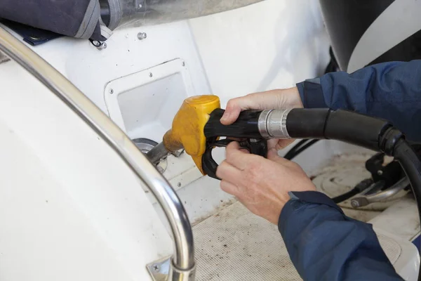 Hands with yellow fuel gun in motor boat fuel filler socket on gas station, watercraft refueling on water