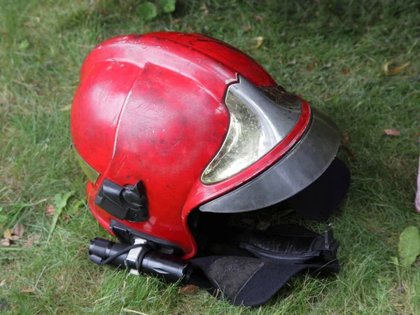 Old red fireman helmet with side flashlight on green grass background, traditional fireman equipment