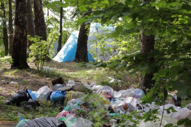 Ormandaki büyük çöp yığını kamp çadırının yanında güneşli bir yaz gününde Park 'taki yeşil ağaçların arasında, plastikler yaban hayatını gezginlerle dolduruyor.