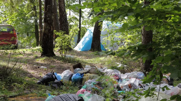 Güneşli bir yaz gününde ormanda kamp çadırının ve arabanın yanında büyük bir çöp yığını. Çevreyi turistlerle dolduran sosyal sorunlar.