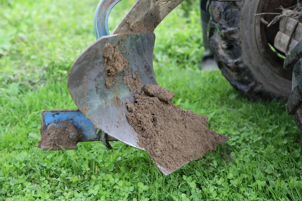 Detachable plow on Walk-behind tractor cleaning with water stream on green grass background, auxiliary tractor parts maintenance, farming mechanization service