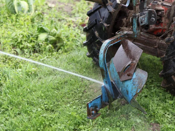 Auxiliary plow on Walk-behind tractor washing with water flow on green grass background, mini tractor parts service, farming mechanization maintenance