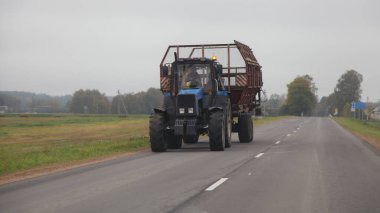 Eski Sovyet tekerlekli traktörü boş saman karavanıyla bir yaz günü yükleme, ön görüş ve tarım işi aracı için asfalt yola çıkıyor.