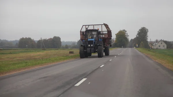 空の干し草トレーラー付きの古いロシアの車輪付きトラクターは ロード フロントビュー 農業農業機器のための秋の日に田舎の空のアスファルト道路上を移動します — ストック写真