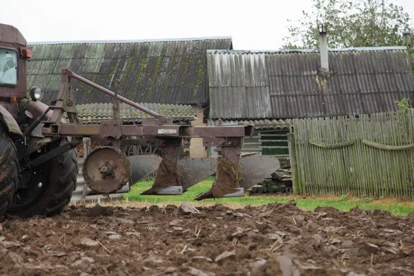 茶畑を耕すトラクターが横に広がる古い三重金属製のプラウ 田舎の木造納屋や風化フェンスの背景に秋の日の土壌栽培 田舎の農業農場 — ストック写真