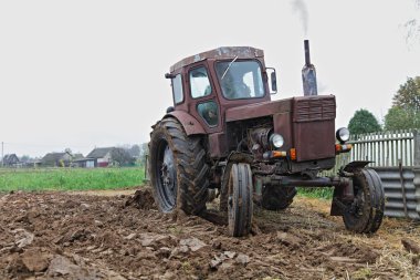 Eski Sovyet 4x4 tekerlekli kahverengi dizel traktörü tarlayı tarlasıyla tarlaya sürerken ön bahçeye yakın, sonbahar günü toprak ekimi, endüstriyel tarım arazisi.