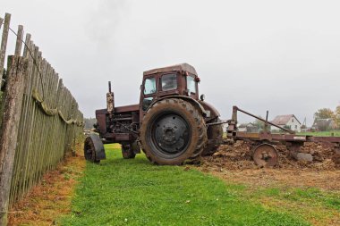 Eski Rus tekerlekli kahverengi traktörü ahşap çitlerin yakınındaki tarlayı sürüyor, bir sonbahar günü toprak ekimi, kırsal tarım manzarası