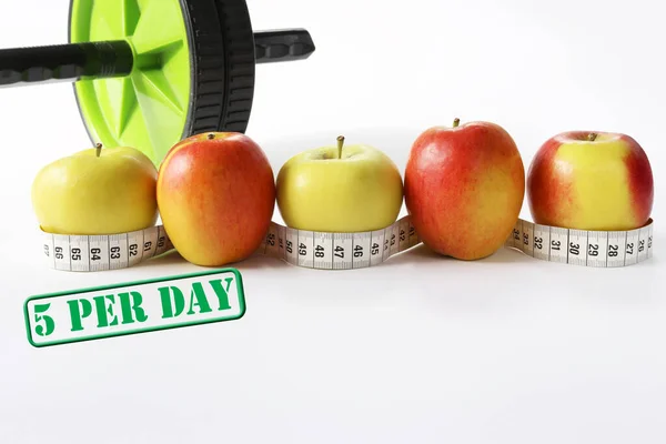 Healthy life concept. Multicolored apples with measure tap and ab wheel on white background