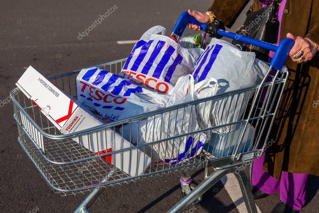 London, UK, November 19, 2011 : Customer shopper pushing a shopping trolley cart full of plastic carrier bags at its Tesco Extra supermarket retail business store in Brent Park Wembley stock photo