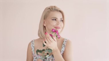 Parlak bir arka planda mavi gözlü güzel, genç, çekici bir kadının portresi bir buket gül tutuyor.