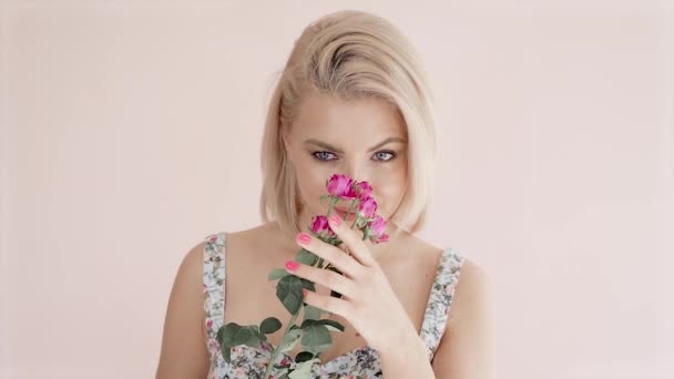 Portrait d'une belle jeune femme blonde aux yeux bleus tenant un bouquet de roses et couvrant son visage d'un bouquet, flirte — Video