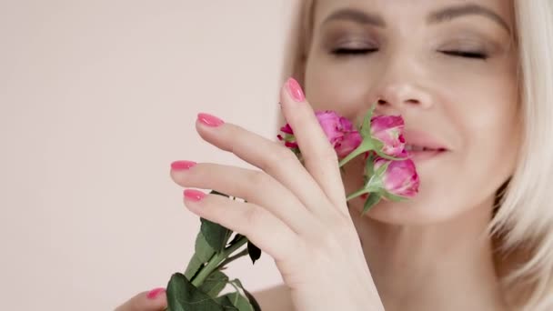Portrait of an attractive young blonde with makeup and a beautiful manicure holding garden roses in her hands, closes her eyes. Tenderness, openness, lightness, flirting — Stock Video