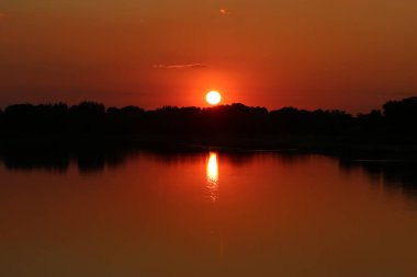 Gölün kıyısında ağaçlarla dolu bir gölde gün batımı.