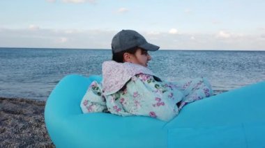 Plajda bir kız şişme bir hamakta oturuyor..