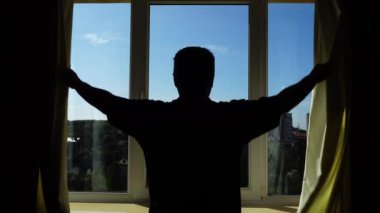Bir adam sabah perdeleri açar ve fiziksel salaklar yapar. Güneş ışınları odaya doğru parlıyor..