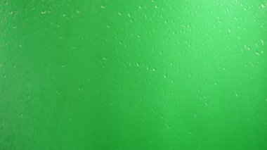 Su damlaları yeşil bir zeminde camdan aşağı akar..