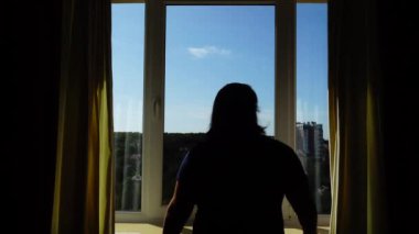 Bir kadın sabah perdeleri açar ve fiziksel dallamalar yapar. Güneş ışınları odaya doğru parlıyor..