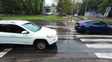 Yağmur sırasında şehir yolu kavşağı. Şehir yollarında ve caddelerde arabalar hareket ediyor. Yaya geçidi ve trafik ışığı.