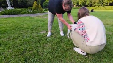 Kadınlar ve kızlar Staffordshire Terrier köpeği ile parkta yeşil çimlerde oynuyorlar..