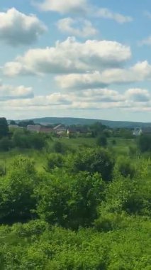 Ev ve ağaçların arka planına karşı kırsalda hareket eden bir tren. Dikey video.