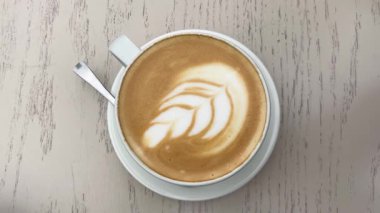 Süt köpüğünde tüy ya da yaprak şeklinde latte sanatı olan bir fincan latte. Güzel bir kahve tasarımının yakın çekimi. Şeker bir kaba doldurulur..