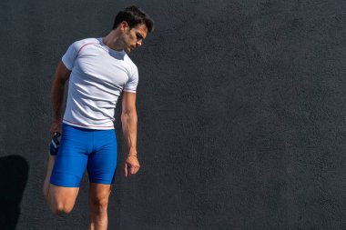 Mavi pantolonlu ve beyaz gömlekli genç adam dinleniyor ve güneşin altında siyah duvarda iyileşiyor, bacak esneme hareketleri yapıyor. Motivasyon konsepti, kariyer
